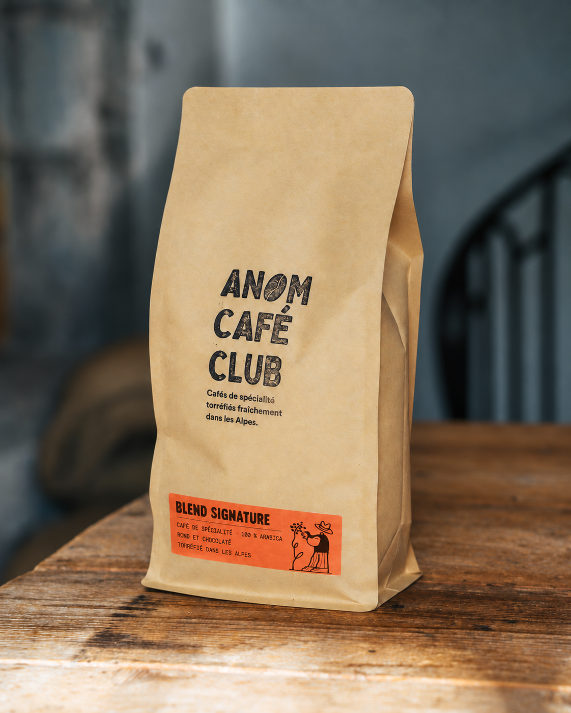 Le sachet kraft ANOM avec son étiquette orange Blend Signature et son illustration de producteur